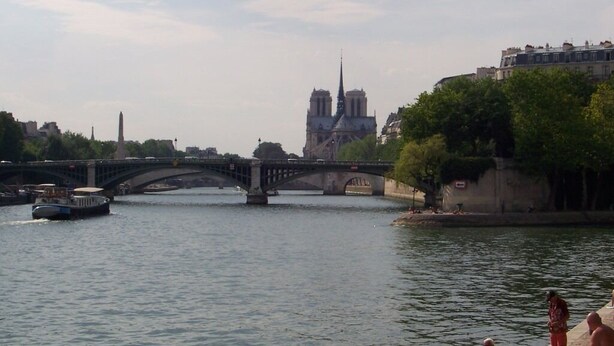 Une rivière avec un pont, un bateau et la cathédrale Notre-Dame en arrière-plan.