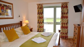 A hotel room with a bed, a wooden dresser, a television, and a view of the outdoors through the door. - Willow Cottage Purpose built wheelchair friendly cottage (Truro)