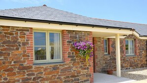 A stone building with a tiled roof, a window with a white frame, and a hanging flower basket. - Willow Cottage Purpose built wheelchair friendly cottage (Truro)