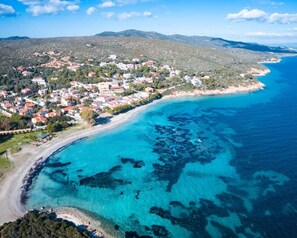 An aerial view of a coastal town with buildings along the shoreline, clear blue waters, and a hilly backdrop. - ISOLA DI SANT'ANTIOCO VILLA WITH GARDEN LOC. MALADROXIA (Maladroxia)