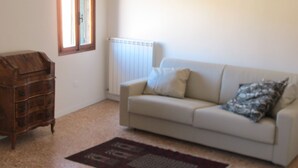 A living room with a white sofa, a wooden chest of drawers, a radiator, and a patterned rug.