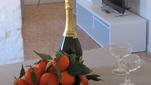 A room with a table displaying a bottle of champagne, a bowl of oranges, and two wine glasses.