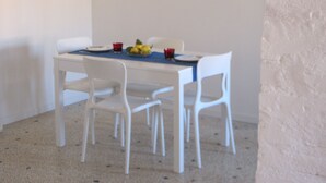 A dining table with white chairs, a blue tablecloth, and a fruit bowl.