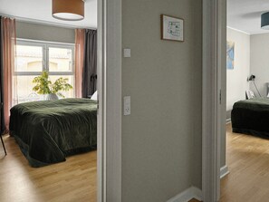 Ein Schlafzimmer mit Bett, einem Fenster mit Vorhängen, einer Pflanze und einer Wandleuchte.