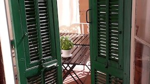 Een uitzicht door groene luiken op een terras met een houten tafel en een plant in pot.