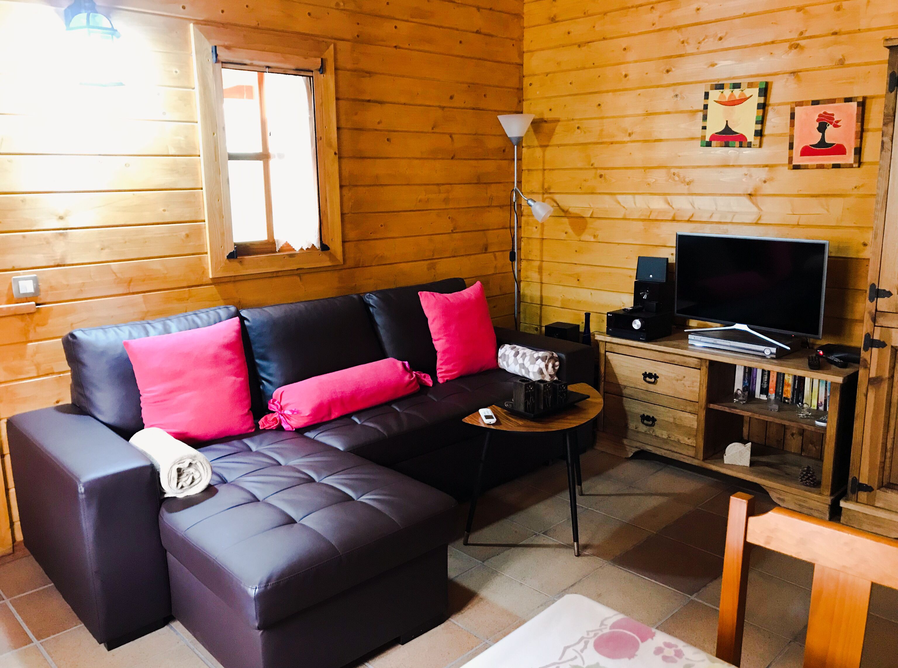 A cozy wooden cabin room with a sectional sofa, a TV, and a small wooden side table.