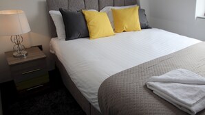 Un lit bien fait, recouvert d’une courtepointe, avec une lampe de chevet et une petite commode.