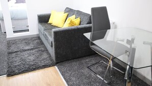 Un salon moderne avec un canapé gris, des coussins jaunes, une table basse en verre et un plancher en bois.