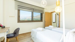 Habitación de hotel con dos camas, un escritorio, una silla y un ventanal con vistas a las montañas.