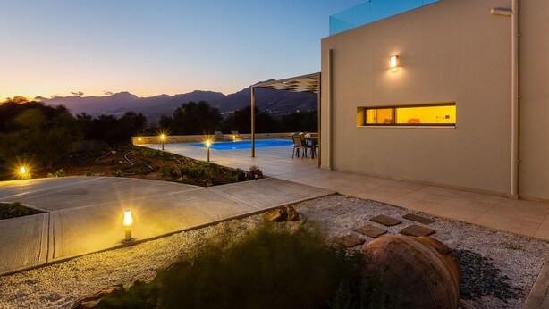 Una casa moderna con piscina, iluminación exterior y vistas a las montañas.