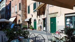 An outdoor cafe with tables and chairs, surrounded by buildings with green shutters and a brick facade. - ARIAS APARTMENT in the iconic Piazza San Michele (Lucca)