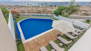 Une piscine avec une terrasse en bois et des chaises longues, offrant une vue sur une plage et l’océan.