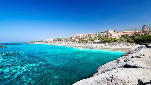 Une ville côtière dotée d’une plage, d’eaux turquoise et limpides, et de bâtiments avec des balcons donnant sur la mer.