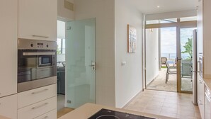 Une cuisine moderne dotée d’appareils électroménagers en acier inoxydable, d’une porte vitrée donnant sur un balcon et offrant une vue sur la mer.