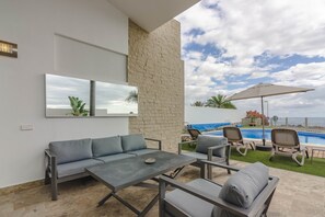 Un espace extérieur moderne, aménagé avec des sièges, une piscine, un mur en pierre et une vue sur l’océan.