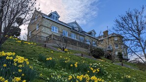 Een groot stenen huis met meerdere balkons en een weelderige tuin vol narcissen.
