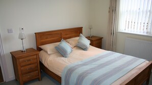 Een opgemaakt bed met een gestreept dekbed, twee nachtkastjes met lampen, en een raam met jaloezieën.