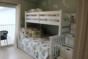 A bunk bed with a patterned bedspread, a chair, and a white wardrobe.