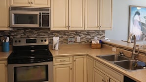 A kitchen with beige cabinets, a microwave, a stove, and a sink. - Villa Sabine by Surfside VR (Pensacola Beach)