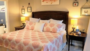 A neatly made bed with a patterned bedspread, two bedside tables with lamps, and framed artwork on the walls. - Villa Sabine by Surfside VR (Pensacola Beach)