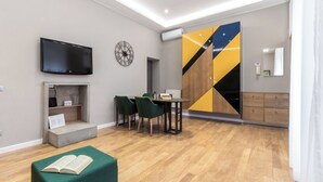 A modern living room with a flat-screen TV, a clock, a dining area with chairs, and a sofa with an open book.