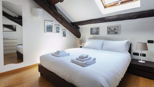A bedroom with a large bed, two bedside tables, a nightstand, a mirror, and a skylight. - Italianway Easy \- Baiamonti 1 (Milan)