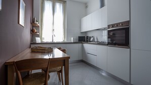 A modern kitchen with white cabinets, a stainless steel oven, a microwave, and a dining table with chairs. - Italianway - Lipari 8 (Milan)