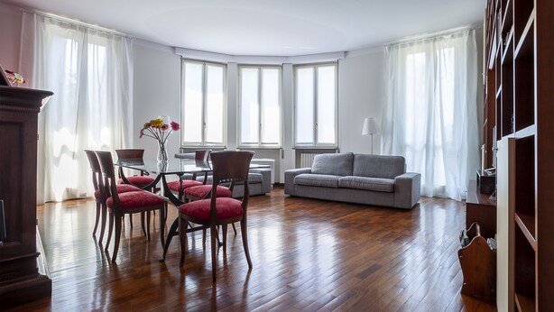 A spacious living room with a wooden floor, a grey sofa, and a dining area with chairs and a table. - Italianway - Lipari 8 (Milan)