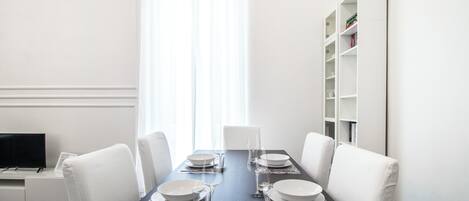 A dining room with a dark wooden table set for four, white chairs, and a white bookshelf against the wall.