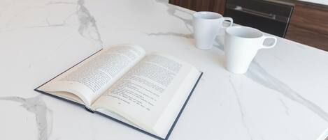 Un livre ouvert sur un comptoir en marbre, avec trois tasses blanches à côté.