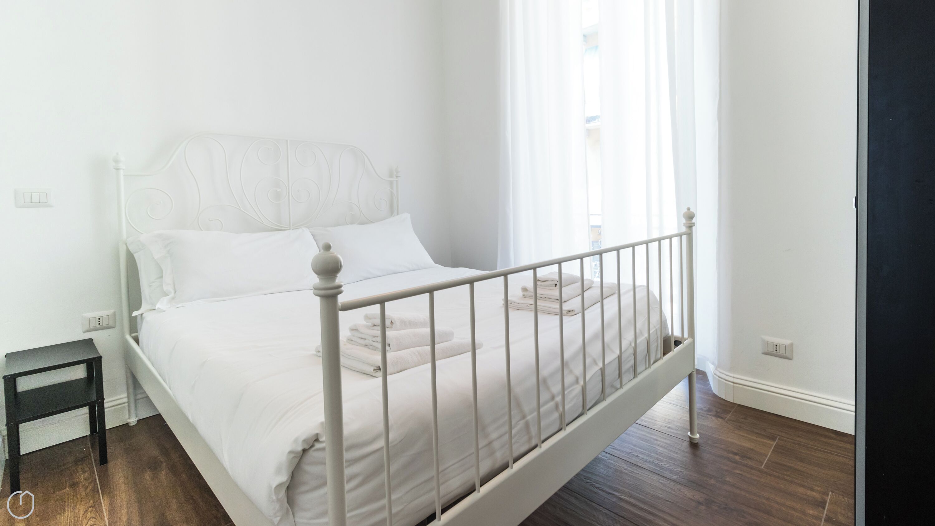 A white bed with a metal frame, white bedding, and a small bedside table.