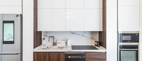 A modern kitchen with a built-in oven, microwave, and dishwasher, along with a marble countertop and wooden cabinets.