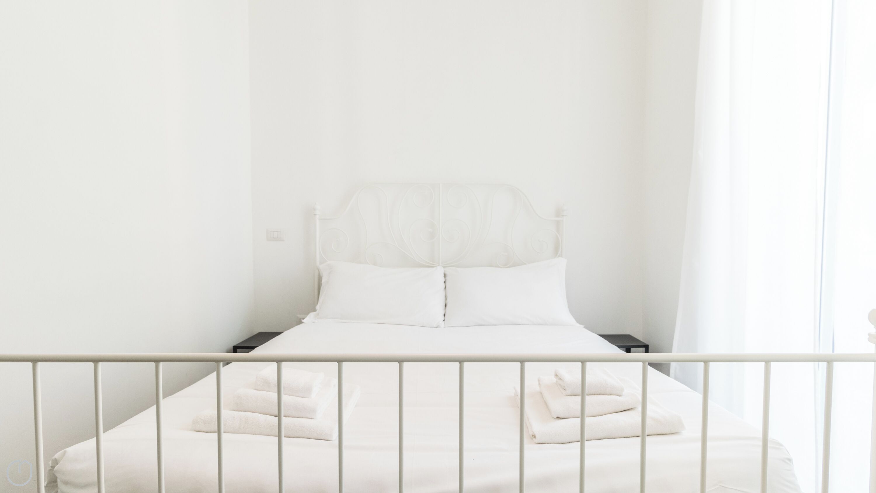 Un lit blanc avec un cadre en métal, des oreillers blancs et des serviettes pliées posées sur le lit.