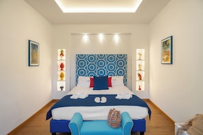 A modern hotel room with a large bed, a blue and white patterned headboard, and a blue bench. - Municipal villa suite (Sorrento)