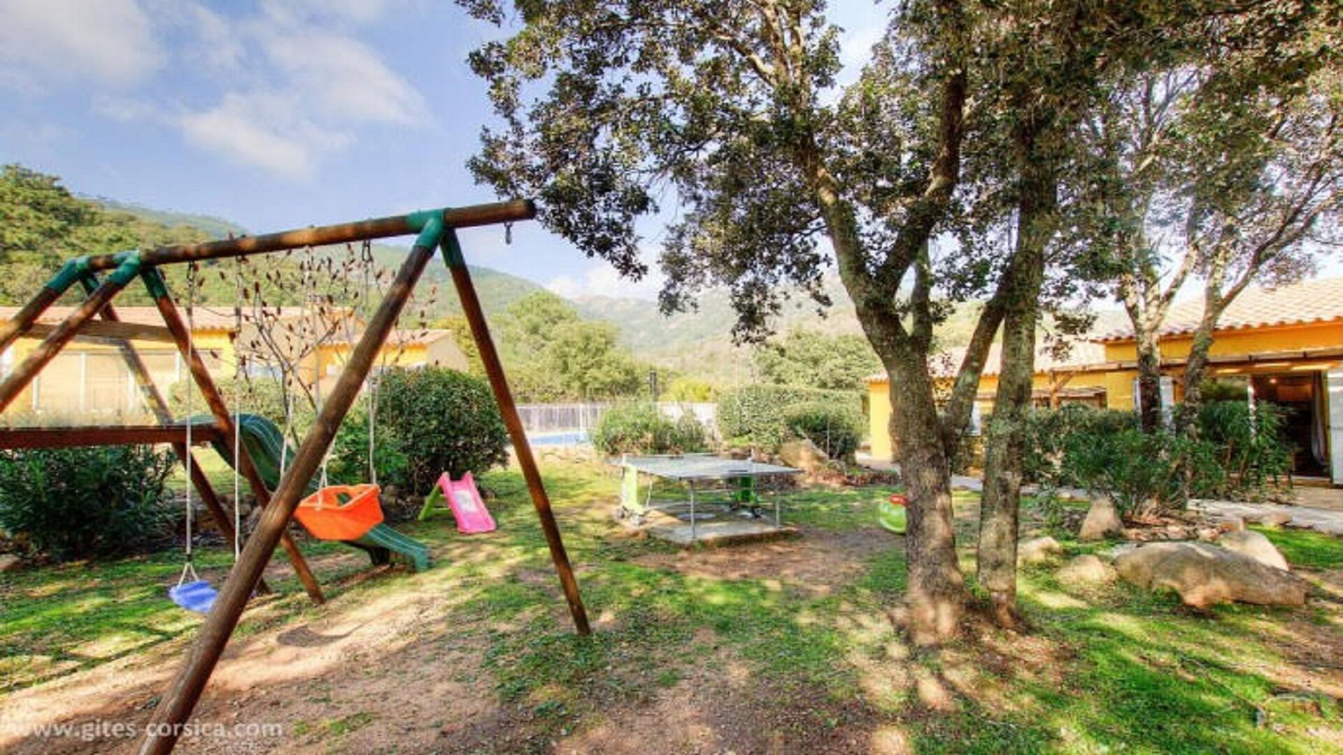 A backyard with a swing set, a table, and a garden.