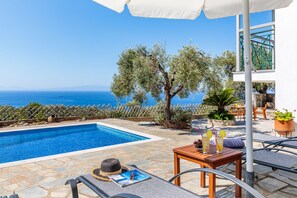 Un espace aménagé au bord de la piscine, avec vue sur la mer, un sol en pierre et du mobilier d’extérieur.