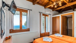 A room with two beds, a wooden ceiling, a window with curtains, a radiator, and a wall-mounted TV. - Villa Glikeria, W/pool, Lovely Sea Views And Close To Everything (Glossa)