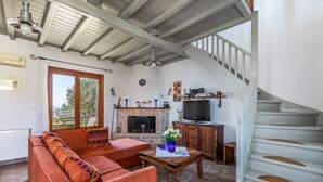 A living room with a sofa, a fireplace, a television, and a staircase. - Villa Glikeria, W/pool, Lovely Sea Views And Close To Everything (Glossa)