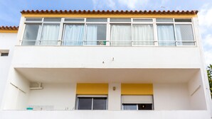 En toetages bygning med balkon, vinduer med gardiner og et tagtækket tag.