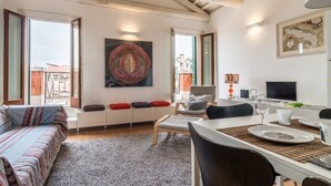 Un salon chaleureux avec un canapé, une table à manger dressée pour deux personnes et un grand tableau abstrait accroché au mur.