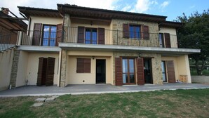 A two-story house with a balcony, stone facade, and wooden shutters.