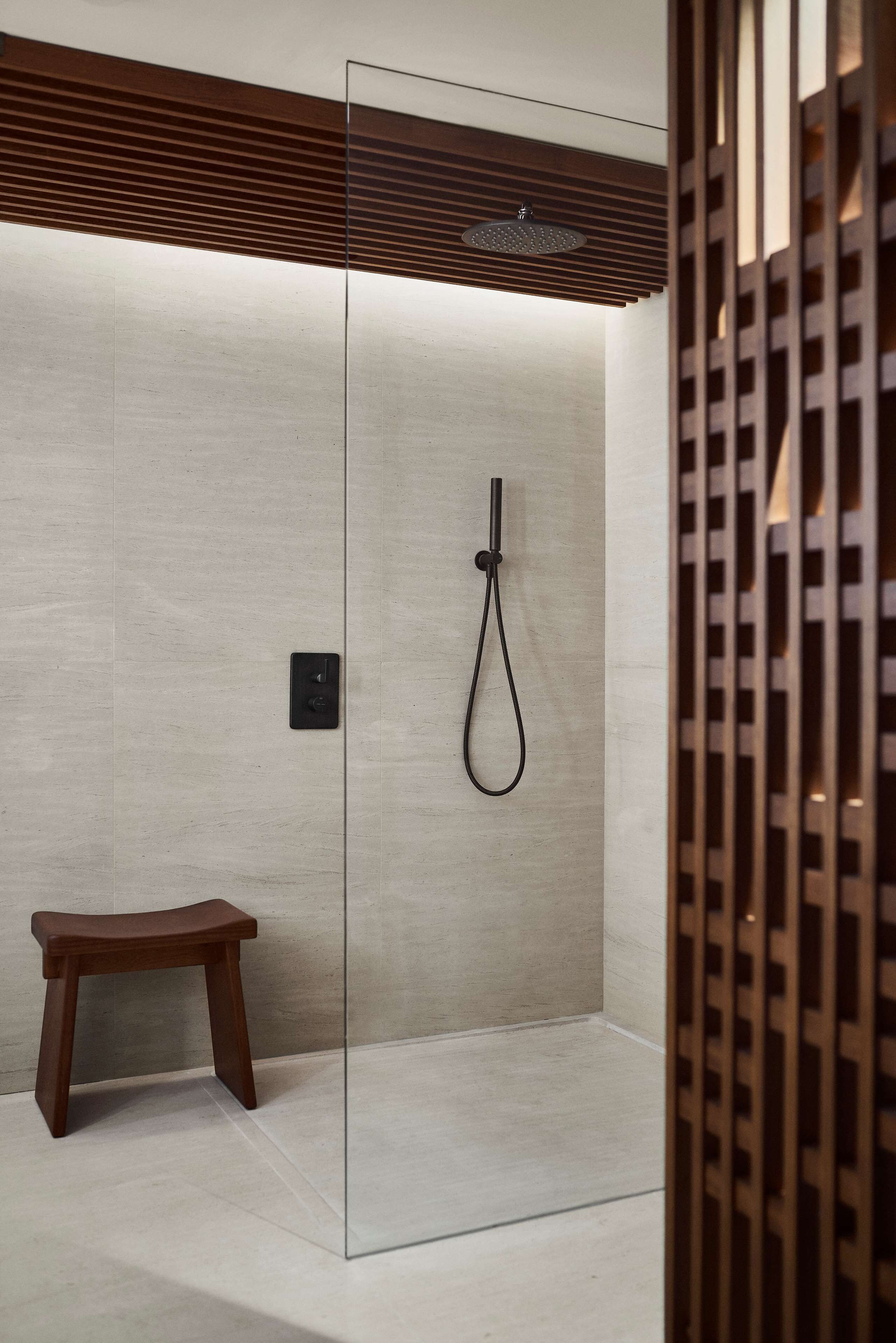 Un área de ducha moderna con mampara de vidrio, banco de madera y ducha empotrada en el techo.