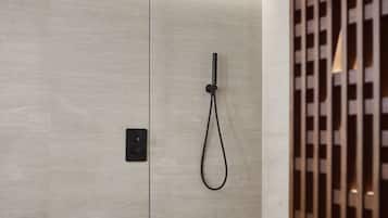 Un área de ducha moderna con mampara de vidrio, banco de madera y ducha empotrada en el techo.