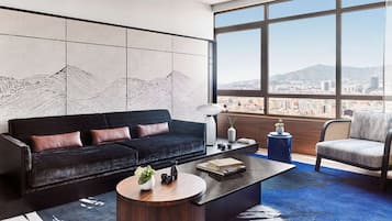 Una sala de estar moderna con un sofá negro, una mesa redonda para café y vistas de un paisaje urbano a través de grandes ventanales.