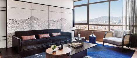 A modern living room with a black sofa, a round coffee table, and a view of a cityscape through large windows.