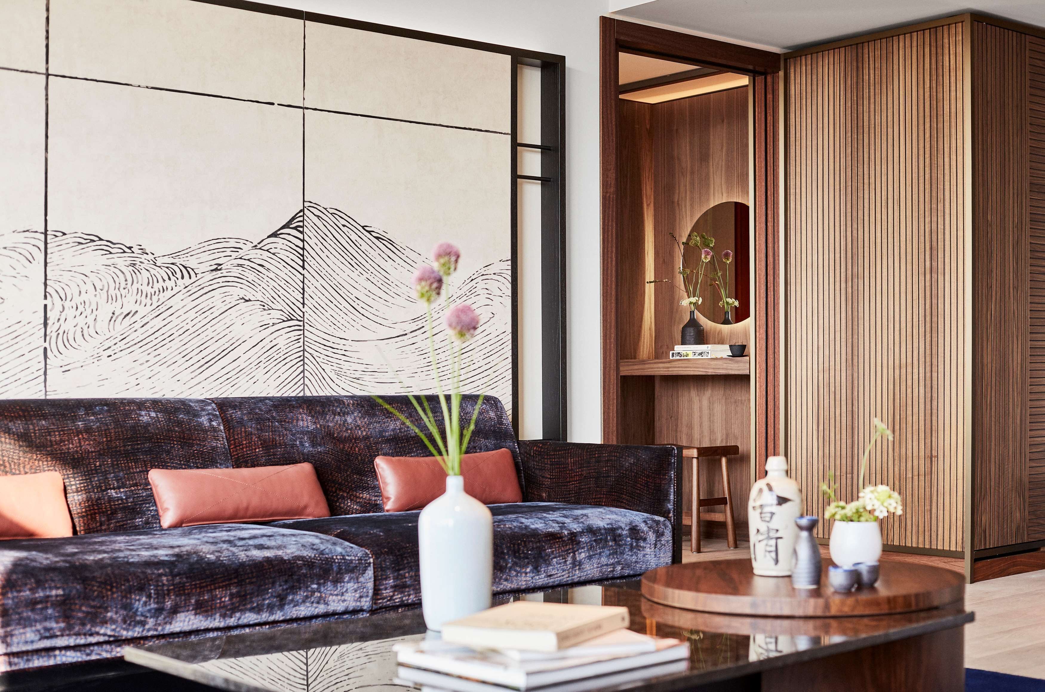 Een moderne woonkamer met een donkere, gestructureerde bank, een ronde houten salontafel en een wandplank met decoratieve objecten.
