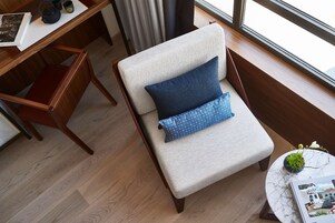 Una zona salotto accogliente e intima, con una poltrona imbottita, un tavolino con una pianta e una finestra con tende.