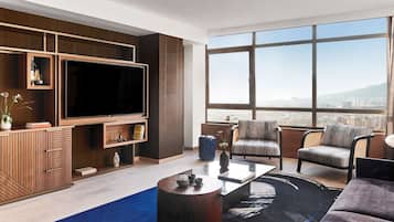 Uma sala de estar moderna com uma televisão grande, assentos confortáveis, uma mesa de centro e vista para a cidade através de grandes janelas.