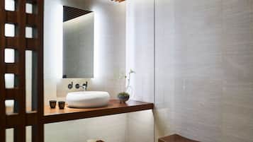 A modern bathroom with a wooden vanity, a white sink, and a small plant.