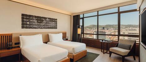 A hotel room with two beds, a view of the city, and a large window.